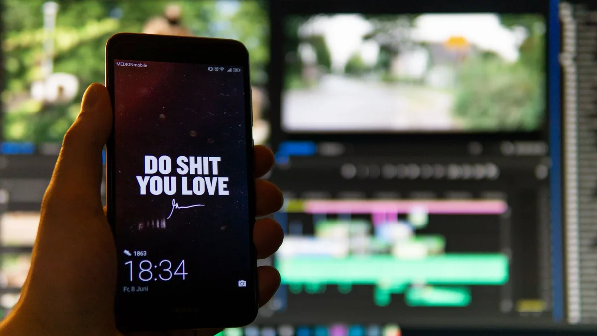 A black smartphone held close to the camera showing a screen against a video editing workspace