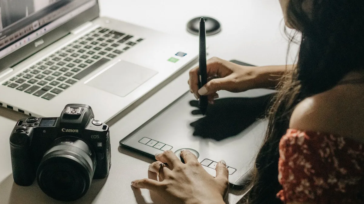 Close-up of someone drawing on a graphics tablet with a stylus next to an open laptop