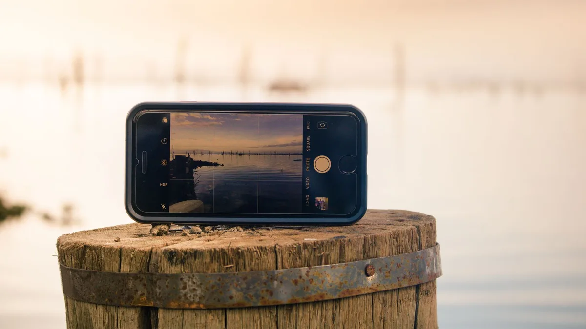 A smartphone held up photographing a lake at sunset, the scene visible on its screen