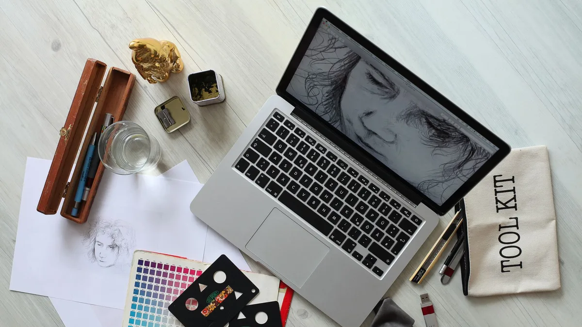 Overhead view of a creative workspace with an open laptop, sketching supplies and a colour palette