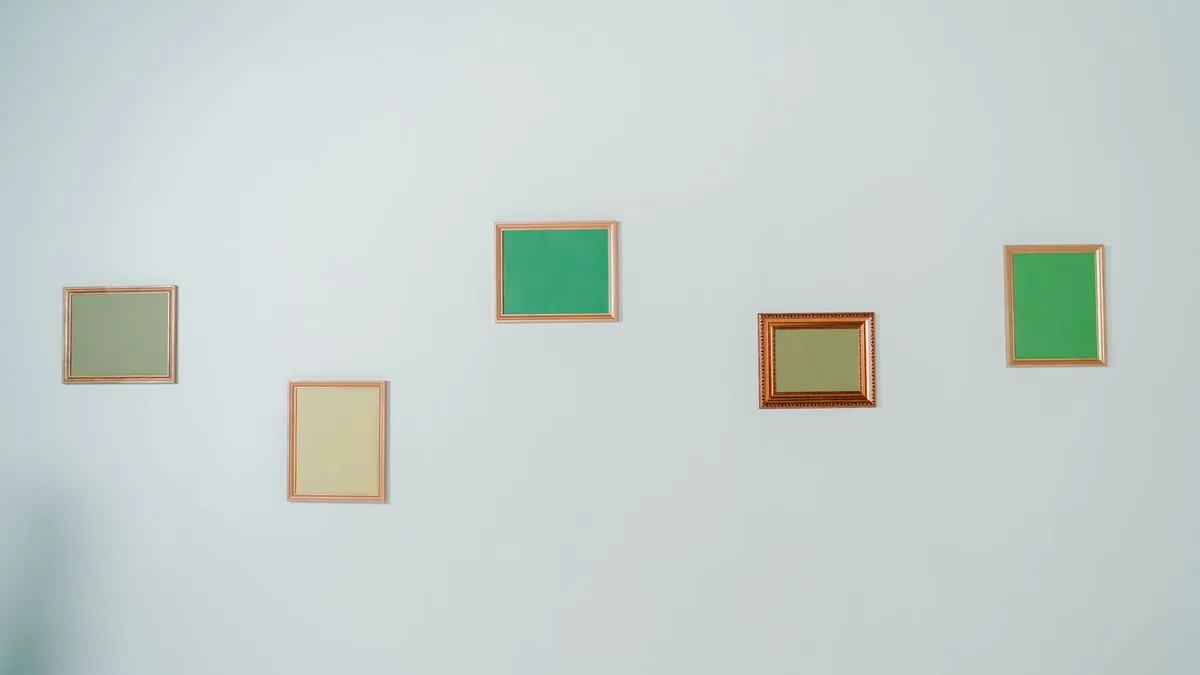 Several empty green picture frames of different shapes arranged on a wall