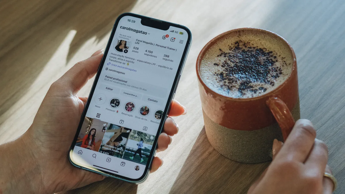 A person scrolling Instagram on a phone beside a cup of coffee on a table