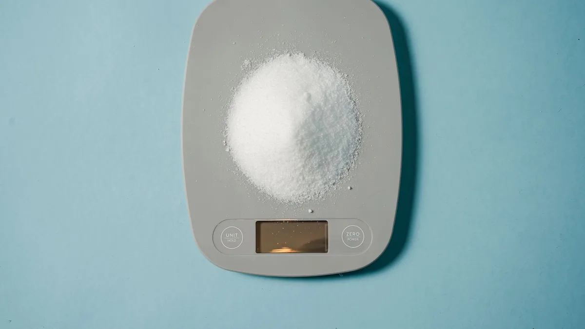 Digital kitchen scales measuring a small heap of sugar against a blue background