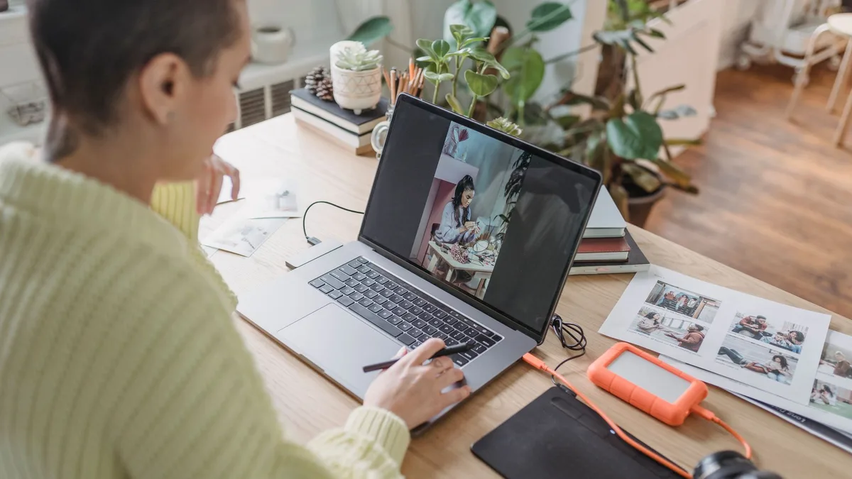 Someone editing photos on a laptop at a table with a graphics tablet and potted plants nearby