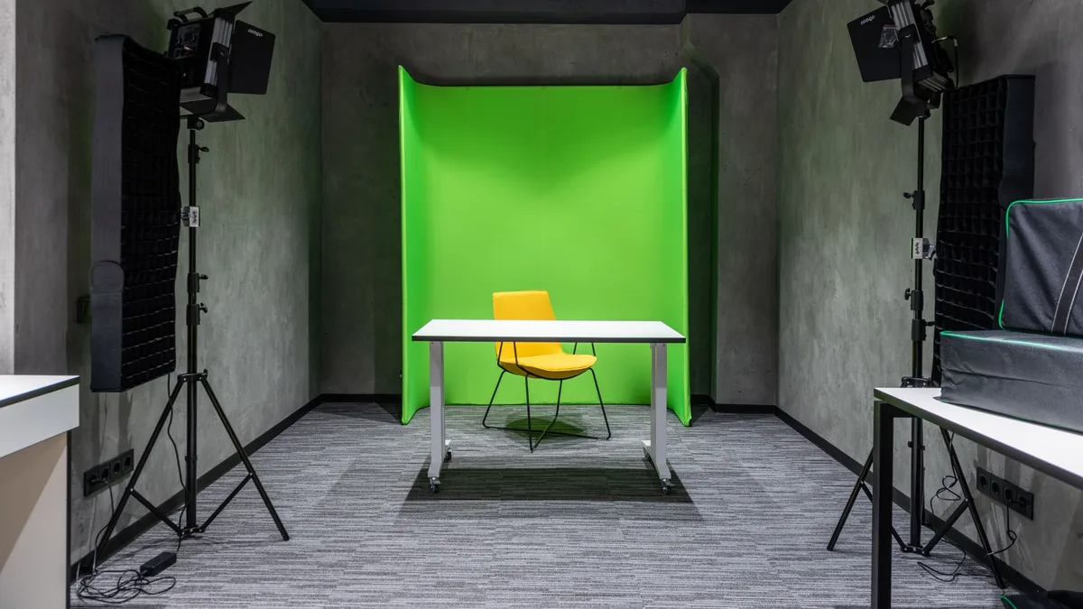 A modern photography studio with a yellow chair and white table set against a plain green wall
