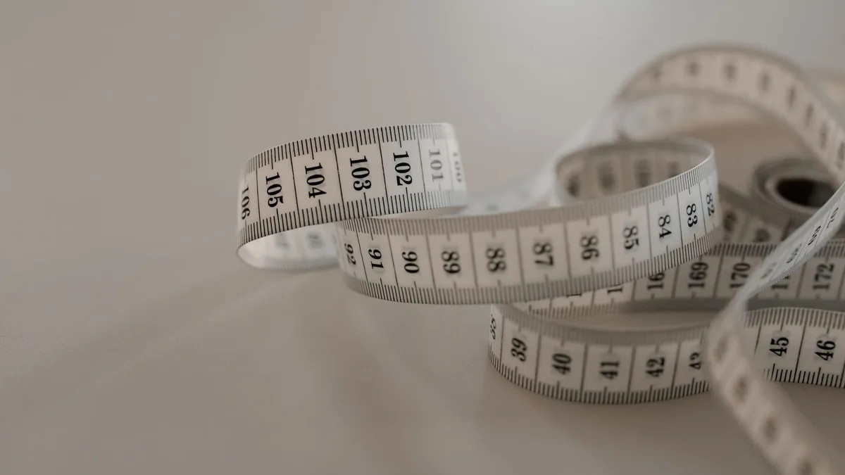 A white tape measure with black numbers coiled loosely on a plain surface